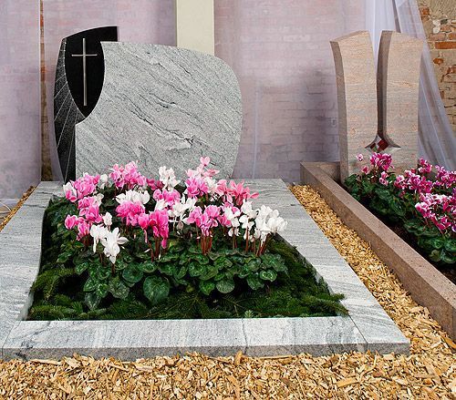 Doppelgrab mit rundem, hellgrauem Stein und pink-weißer Blumenbepflanzung